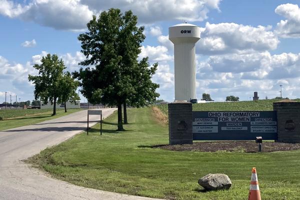 Blue sky, puffy clouds, green grass all framed around the Ohio Reformatory for Women sign