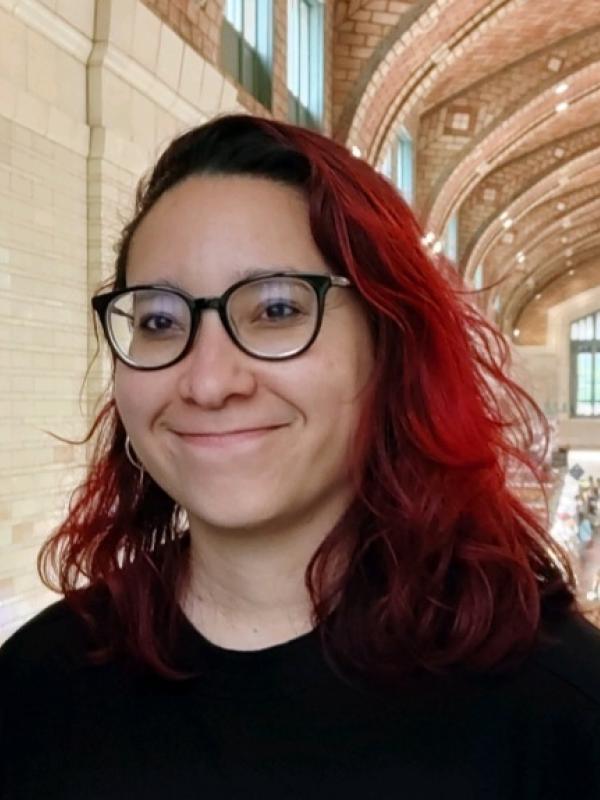 Red-haired femme presenting person with black glasses and black sweatshirt.