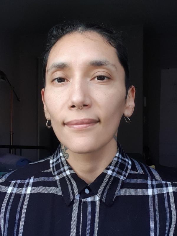 Portrait of a person with black hair, brown eyes, two hoop earrings and a blue plaid shirt.