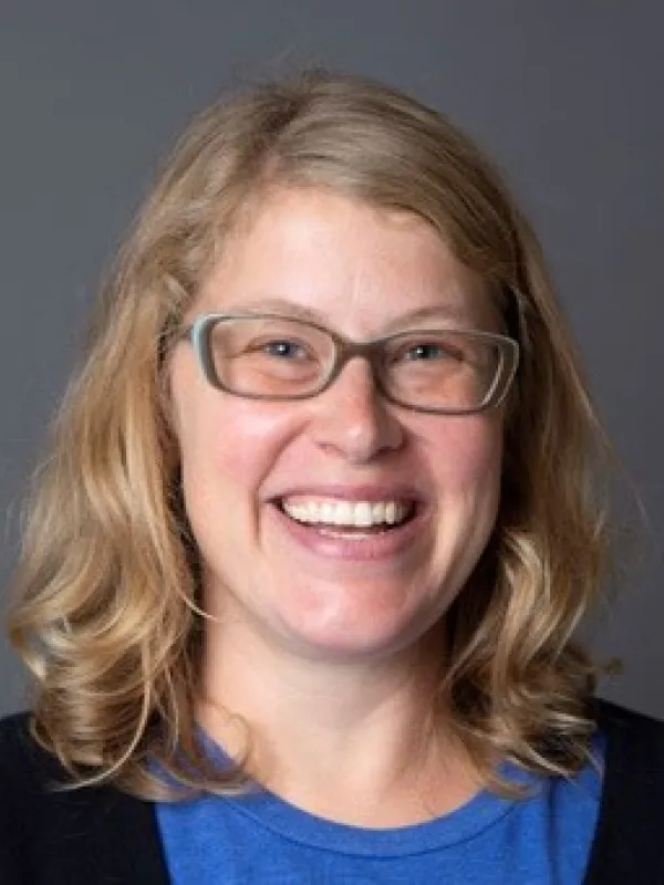 Smiling white woman with blonde hair, glasses, and a blue shirt.