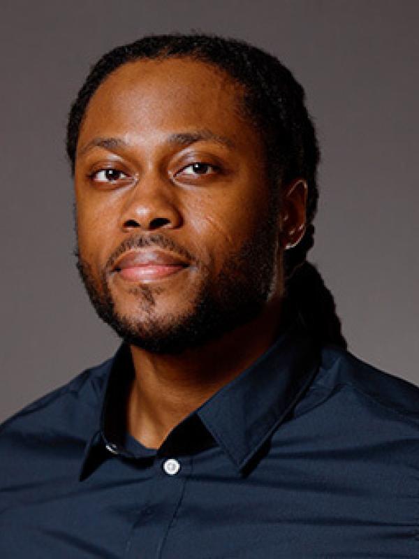 Man with brown skin, brown eyes, and dark brown hair wearing a blue shirt.