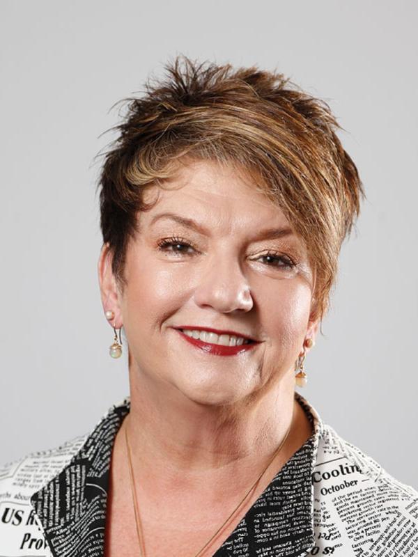 Smiling white woman with short brown hair, red lipstick, and a white blouse.