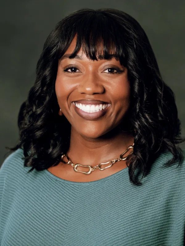 Black woman with bangs and shoulder-length hair, gold necklace and teal sweater.