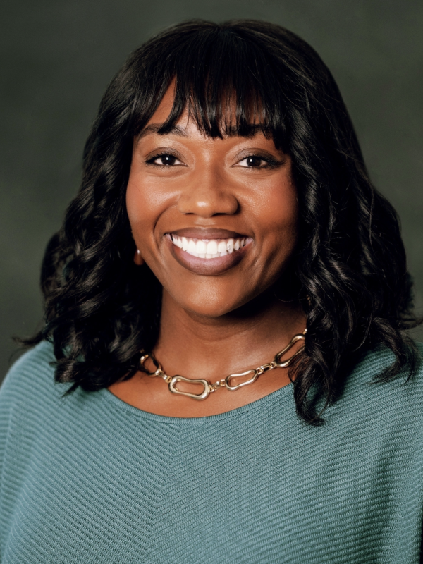 Black woman with bangs and shoulder-length hair, gold necklace and teal sweater.